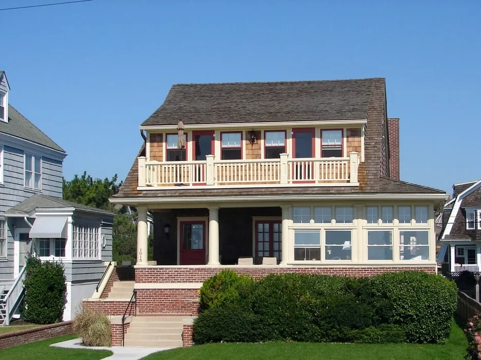 A shingled New England house with a deep covered porch, cream window trim and brick front steps, photographed after a full exterior repaint.