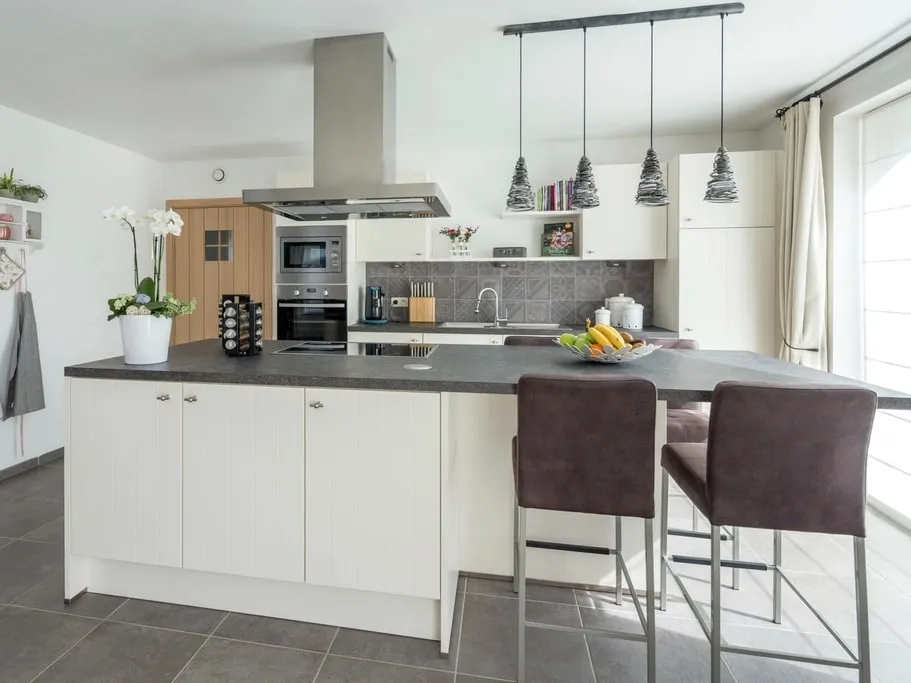 A kitchen with cabinet doors refinished in a sprayed off-white, with a dark stone worktop and island.
