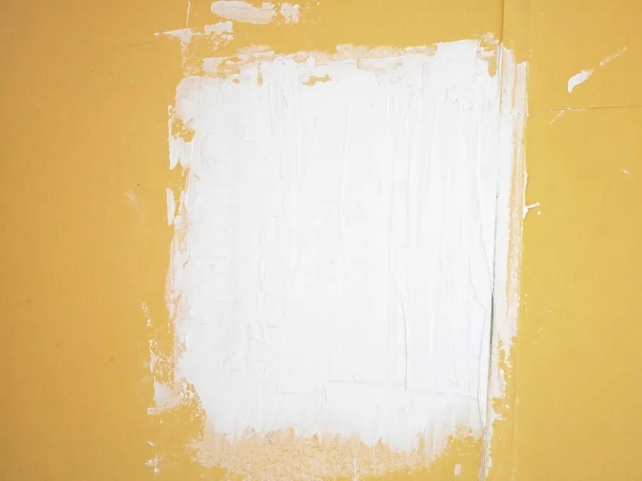 A patch of fresh white filler skimmed flat over a yellow wall, sanded and waiting for primer.
