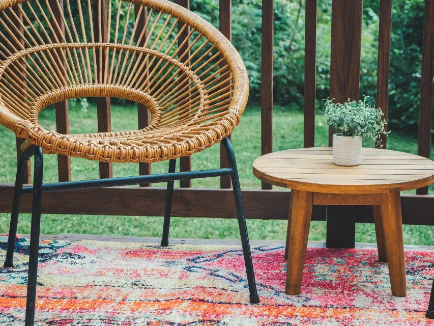 A back porch with a stained timber railing, looking out over a garden, with chairs and a low table.